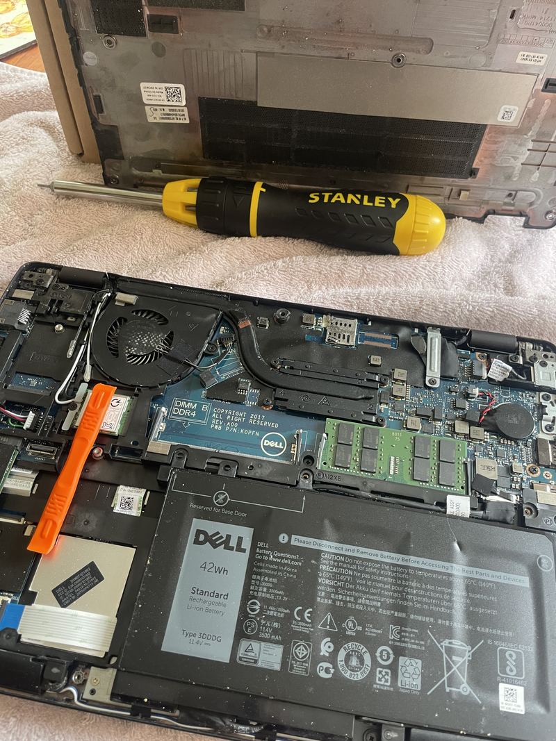 A Dell Latitude 5290 on a towel with its base removed: the fan and heatsink at the top, the memory module and wireless card in the middle, and the original 42 Wh battery still fitted across the bottom.