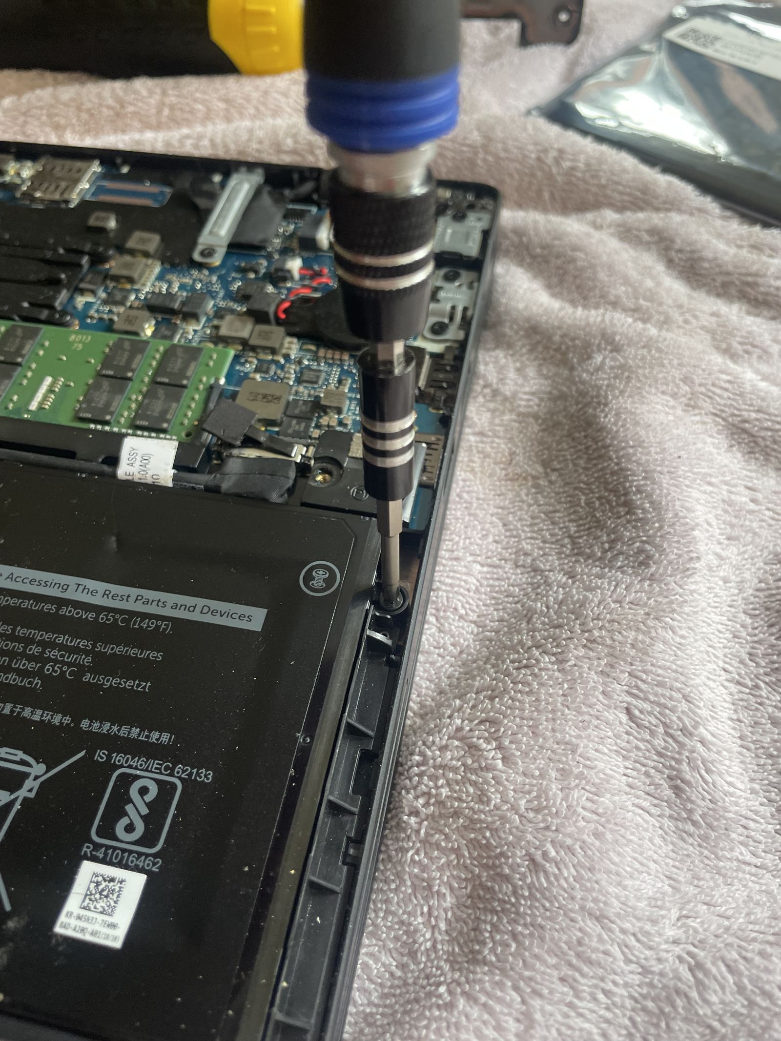 A precision driver on one of the screws at the edge of the battery, the memory module and board above it.