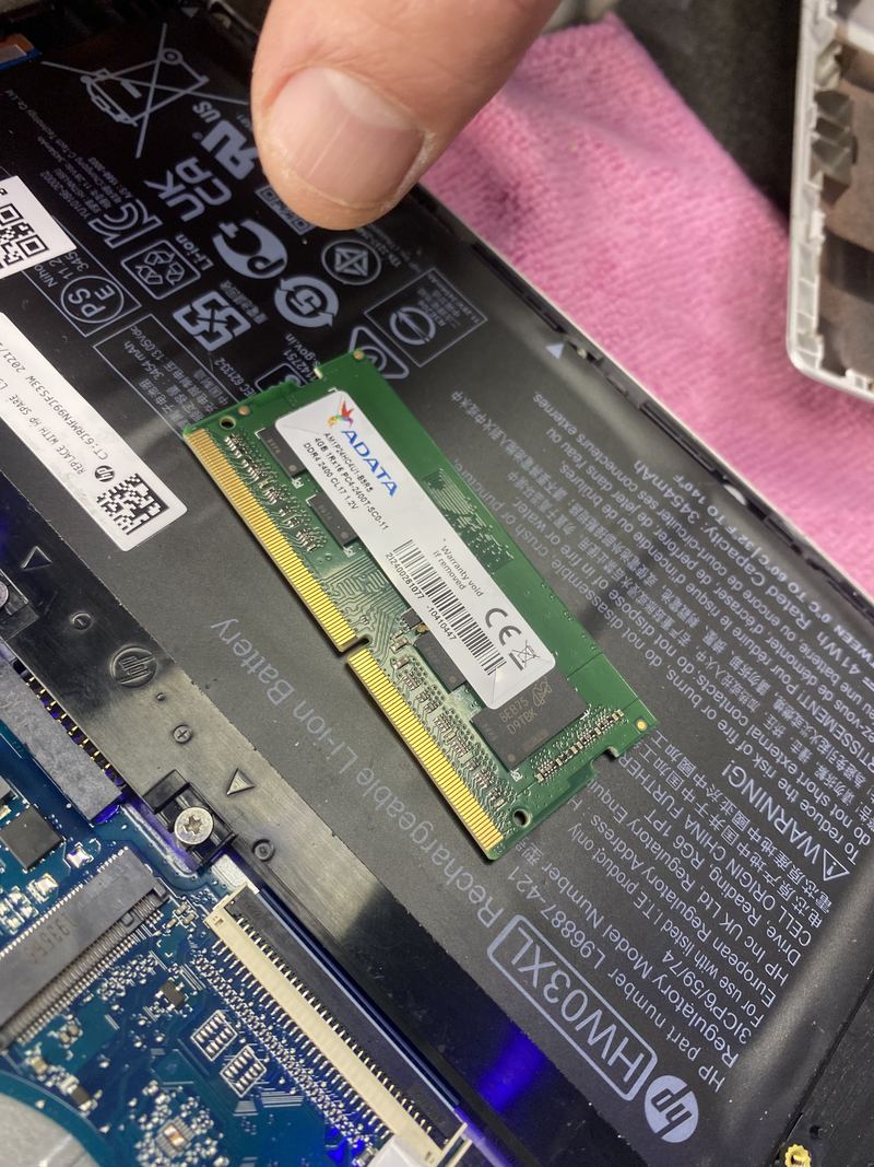 A memory module held above the opened underside of an HP laptop, ready to be fitted.