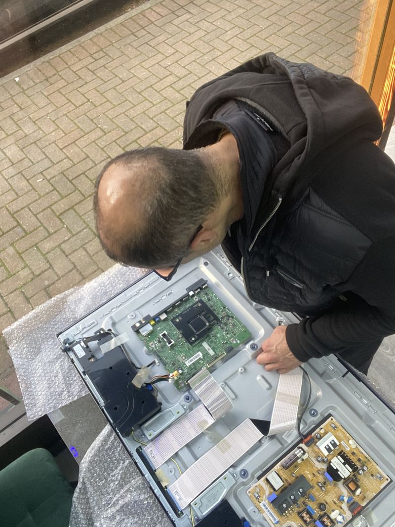 A JorTech technician bent over the opened rear panel of a television, working on the exposed mainboard.