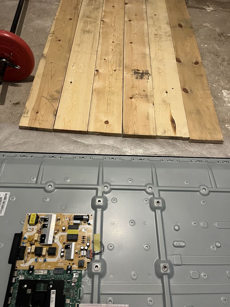 A television laid flat and face down, stripped back to the grey metal chassis, with the power board and mainboard in one corner.